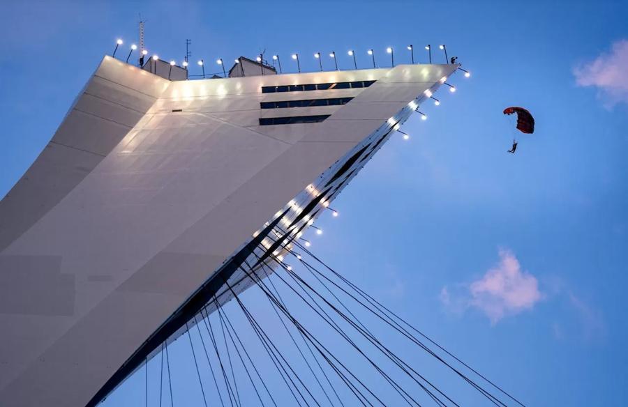 A parachute opens beside the Olympic Stadium tower at dusk