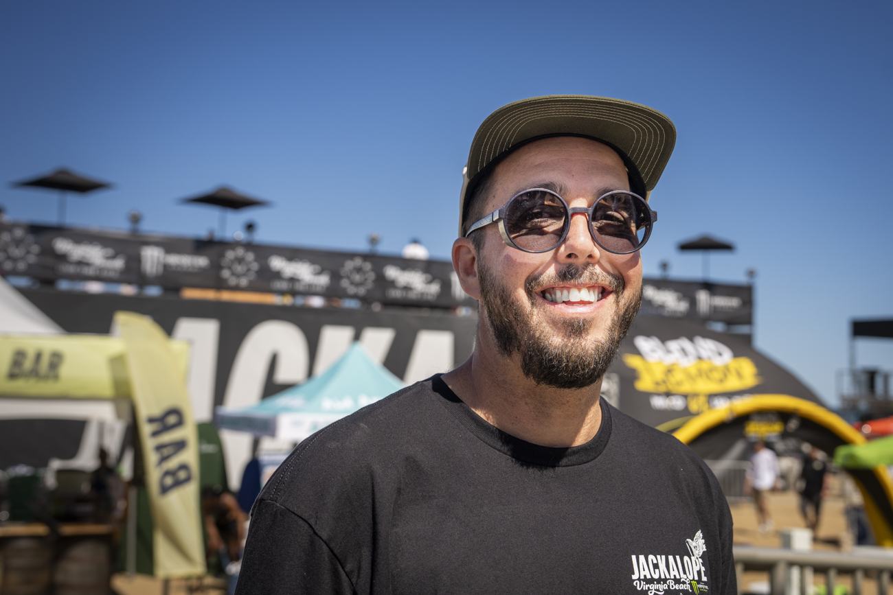 Micah smiling in a cap and round sunglasses in front of the JACKALOPE stage at Virginia Beach