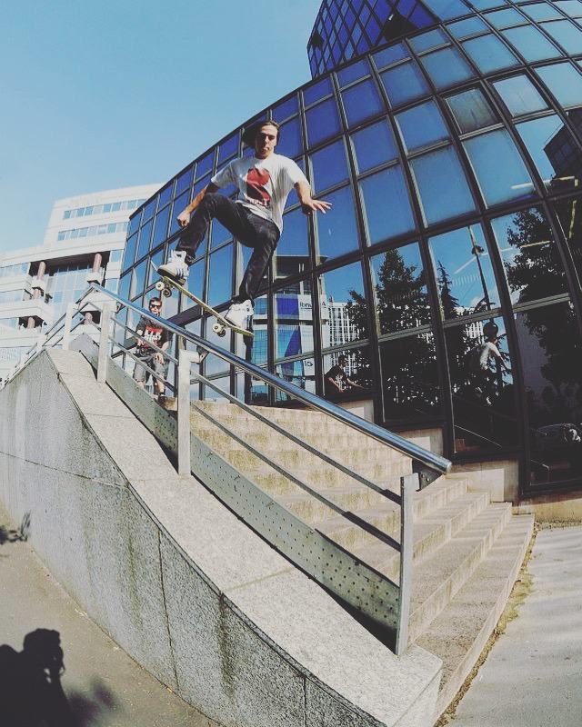 Micah boardslides a handrail down a staircase in Paris, glass tower behind